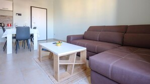A modern living room with a brown leather sofa, a white coffee table, and a dining area with a white table and chairs. - VillaRealeFlats (Lecce)