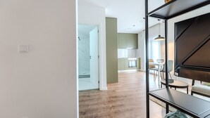 A modern interior with a wooden floor, a dining area with a table and chairs, and a kitchen with cabinets and a hanging light. - LZ Studio by House and People (Braga)
