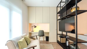 A modern living room with a sofa, a TV on a black stand, a desk with a lamp, and a bookshelf. - LZ Studio by House and People (Braga)