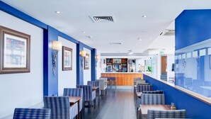 Un restaurante con paredes azules, mesas y sillas de madera. Se ve una zona de bar al fondo.