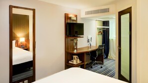 Una habitación de hotel con una cama, un escritorio con una silla, un televisor y un armario.