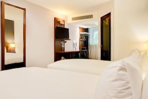 Une chambre d’hôtel comprenant un lit, un bureau avec une chaise, une télévision, un porte-manteau et une porte.