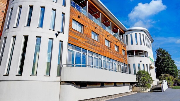 Un edificio moderno con una combinación de fachada blanca y de madera, ventanas grandes y una sección de esquina curva.