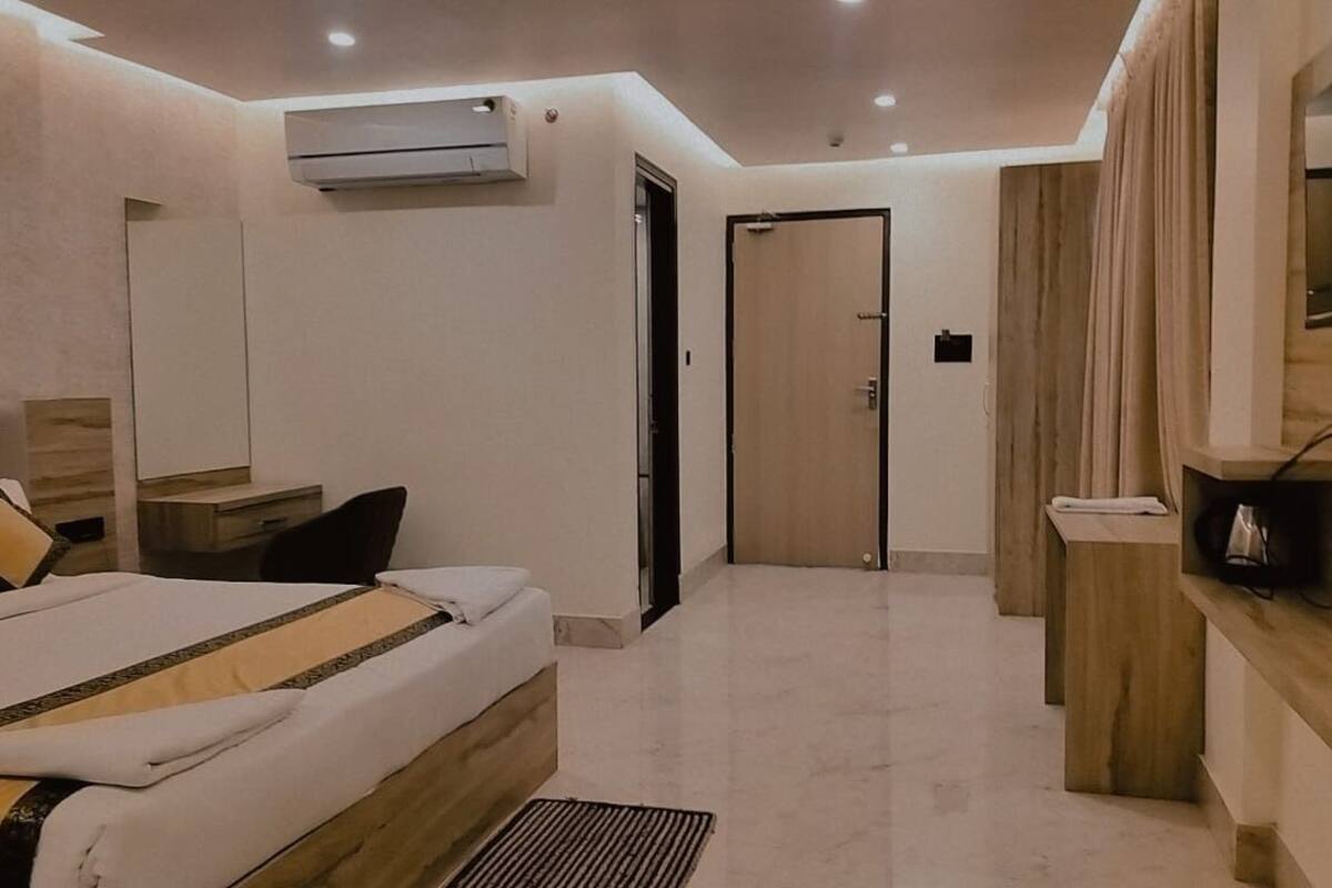 A modern hotel room with a bed, bedside table, TV, and a wooden bench.