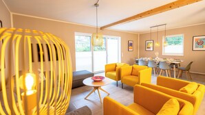 Un salon moderne avec des canapés jaunes, un coin repas avec une table et des chaises, et de grandes fenêtres laissant entrer la lumière naturelle.