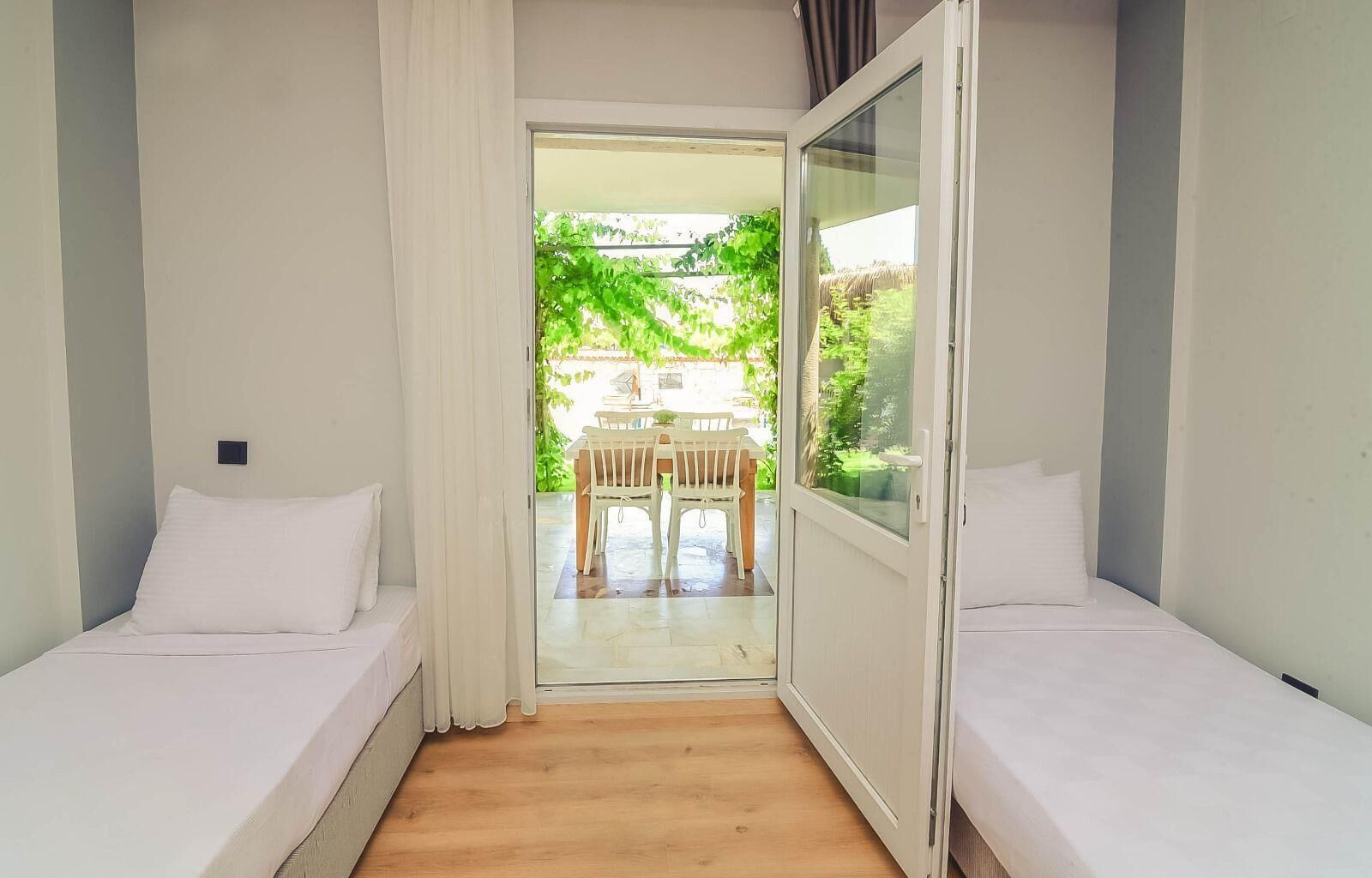 A room with two beds, a wooden floor, and a view of an outdoor patio with a table and chairs.