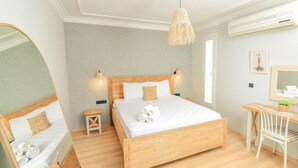 A bedroom with a wooden bed, bedside tables, a desk, a chair, a hanging light fixture, and a wall-mounted air conditioner. - Gerence Alacati  (Cesme)