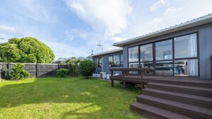 A modern building with large windows, a wooden deck, and a grassy yard.