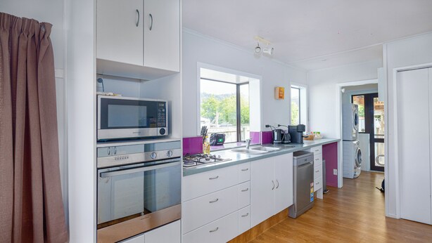 A modern kitchen with white cabinets, a microwave, an oven, a dishwasher, and a window providing a view of the outdoors.