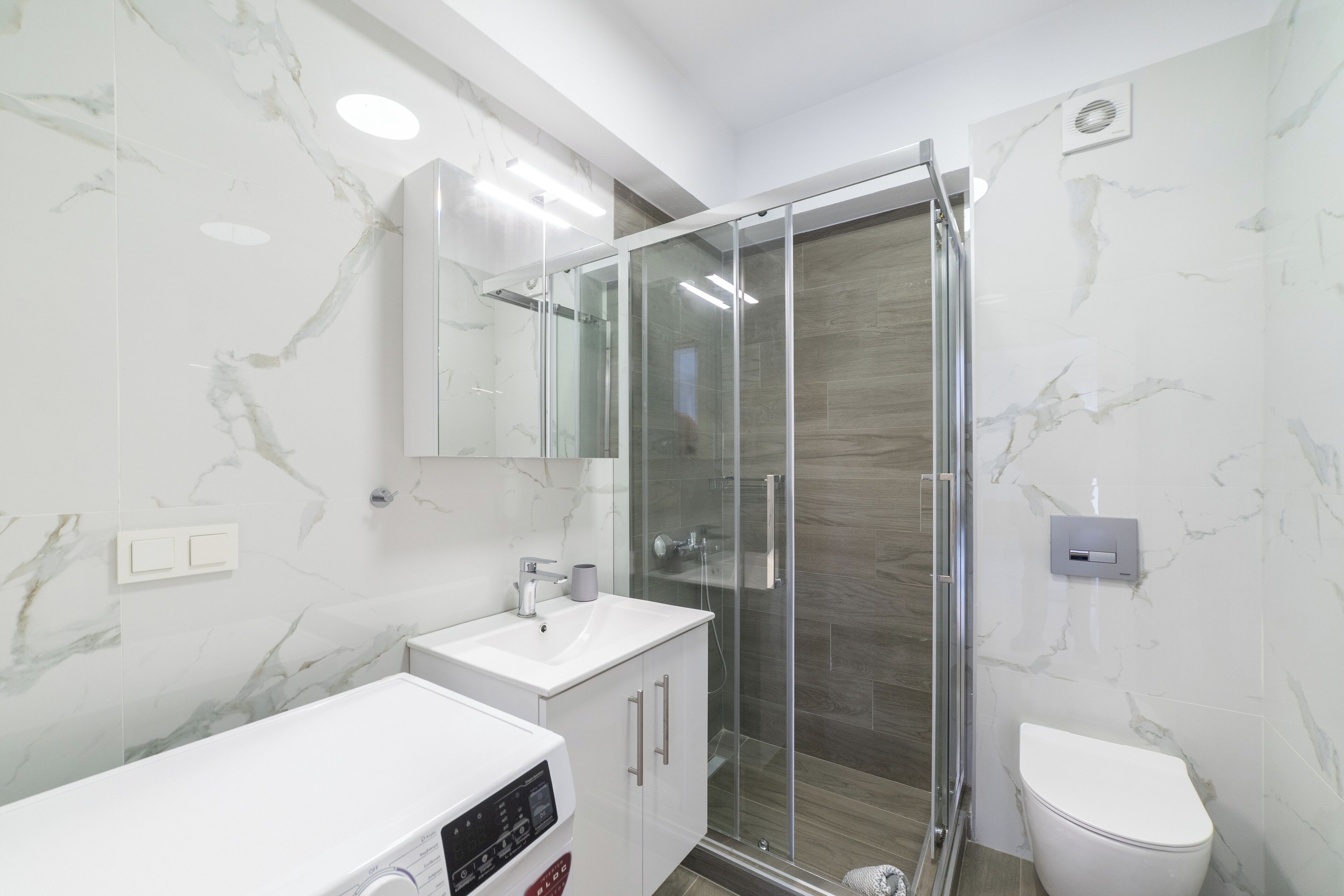 Ein modernes Badezimmer mit einer gläsernen Dusche, einem weißen Waschbecken und einer Toilette.