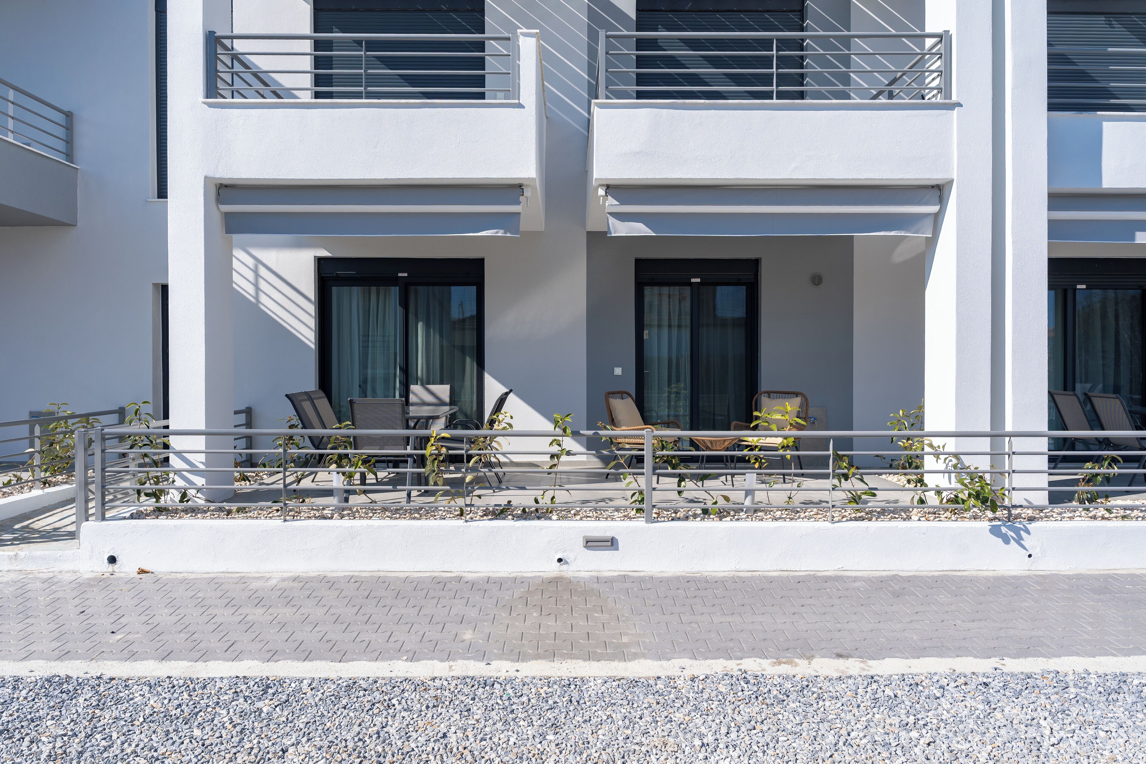 A modern two-story building with a balcony, outdoor seating, and a gravel pathway.