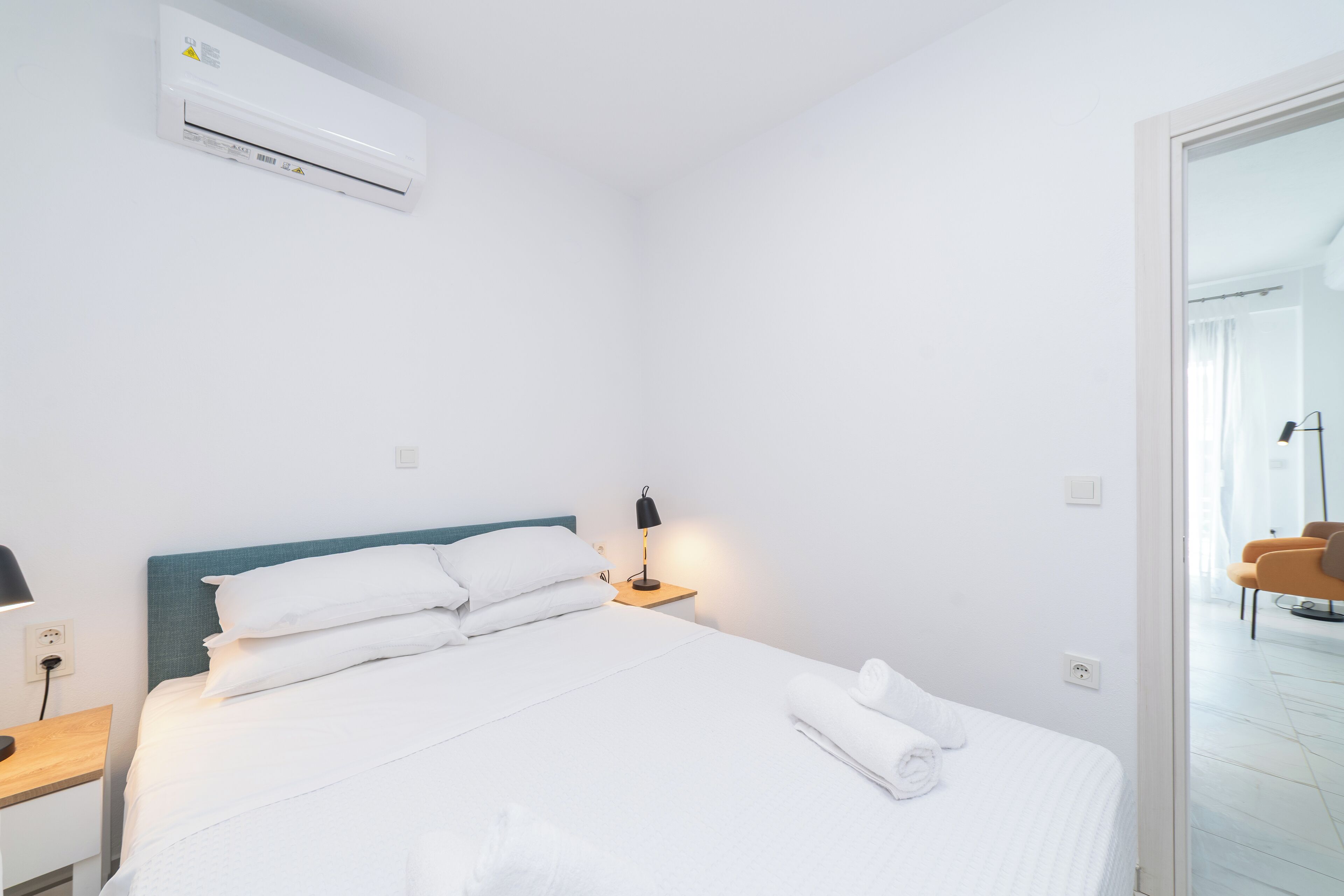Una habitación de hotel con cama, mesita de noche, lámpara y aire acondicionado.