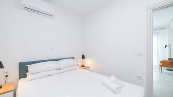 Una habitación de hotel con cama, mesita de noche, lámpara y aire acondicionado.