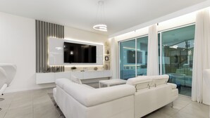 Un salon moderne avec un canapé blanc, un téléviseur à écran plat et une porte vitrée donnant sur un balcon.
