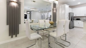 Une cuisine moderne avec des meubles blancs, un réfrigérateur en acier inoxydable et une table à manger en verre, assortie de chaises blanches.