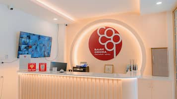 A reception desk with a large screen displaying multiple camera feeds, a sign for Baan Cocoa, and a modern, minimalist interior design.