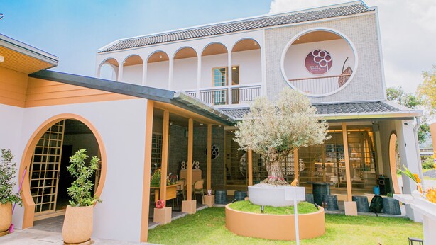 A modern building with a covered patio, large windows, and a circular logo on the facade. - Baan Cocoa Boutique Hotel (Takua Thung)