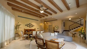 Amplia sala de estar con un sofá grande, sillas de madera, una mesa de comedor y una escalera que conduce a un nivel superior.