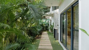 Un sendero estrecho bordeado por abundante vegetación y arquitectura moderna con grandes ventanales.
