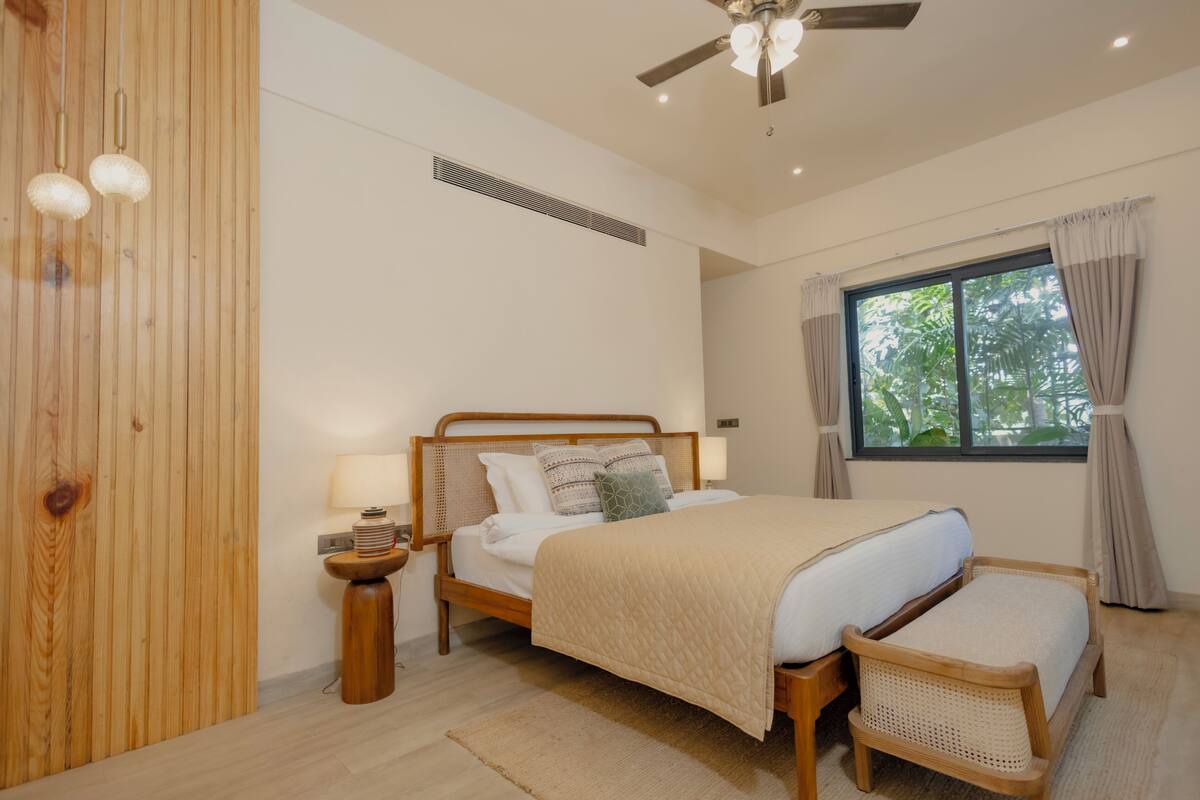 Une chambre à coucher avec un lit en bois, des tables de chevet, une fenêtre avec des rideaux et un ventilateur de plafond.