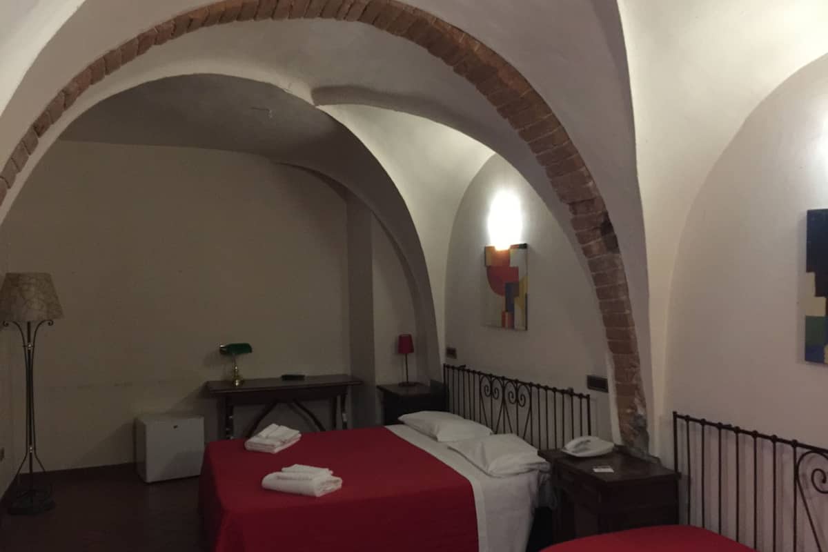 A room with two beds, a desk, a lamp, and a painting on the wall.