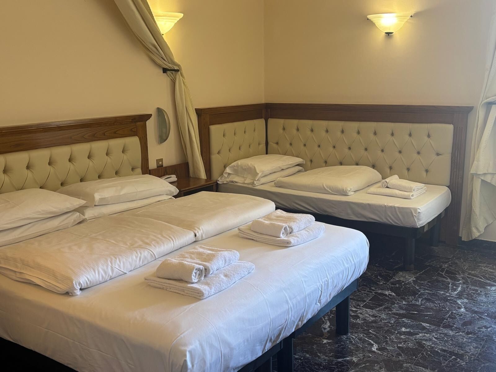 Ett hotellrum med en stor säng, två mindre sängar och ett golv av marmor.