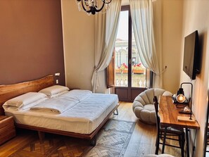 Ein Schlafzimmer mit einem hölzernen Bett, einem Schreibtisch mit Stuhl, einem Fernseher und Blick auf ein Gebäude durch ein Fenster mit Vorhängen.