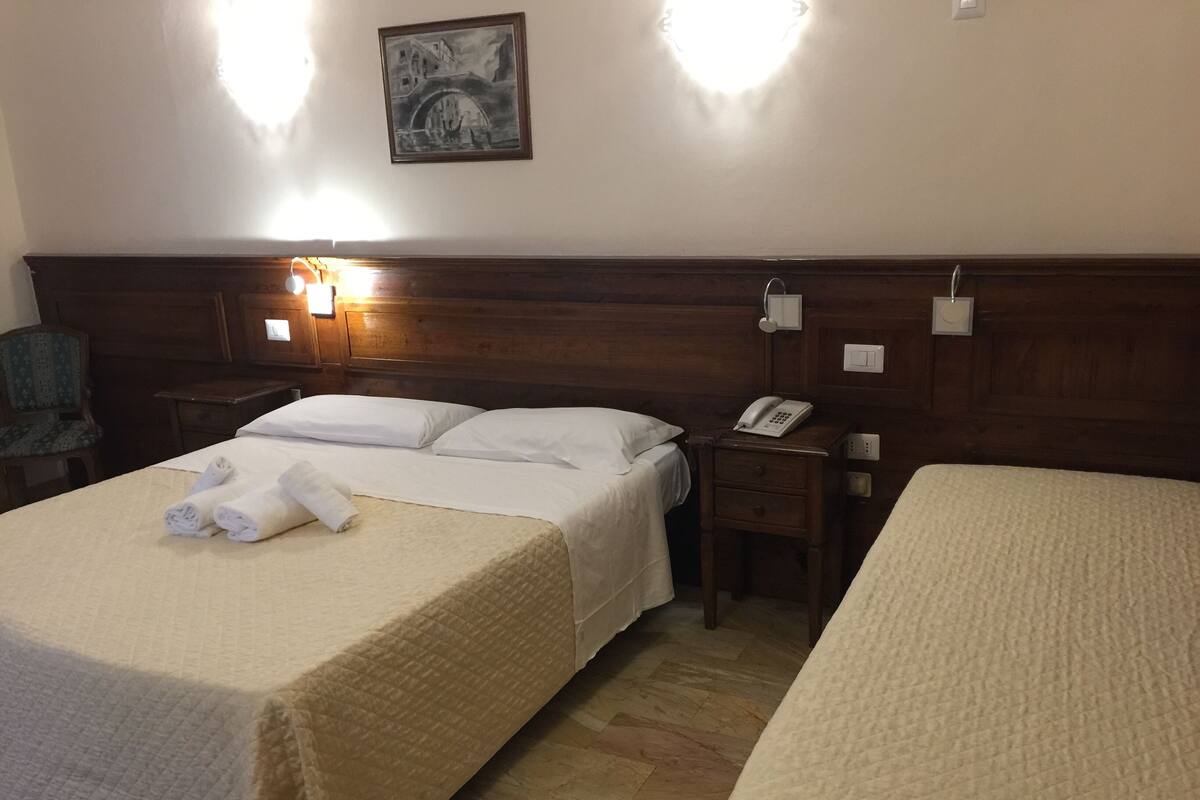 A hotel room with two beds, a wooden headboard, a bedside table with a phone, and a wall-mounted light fixture.