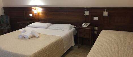 A hotel room with two beds, a wooden headboard, a bedside table with a phone, and a wall-mounted light fixture.