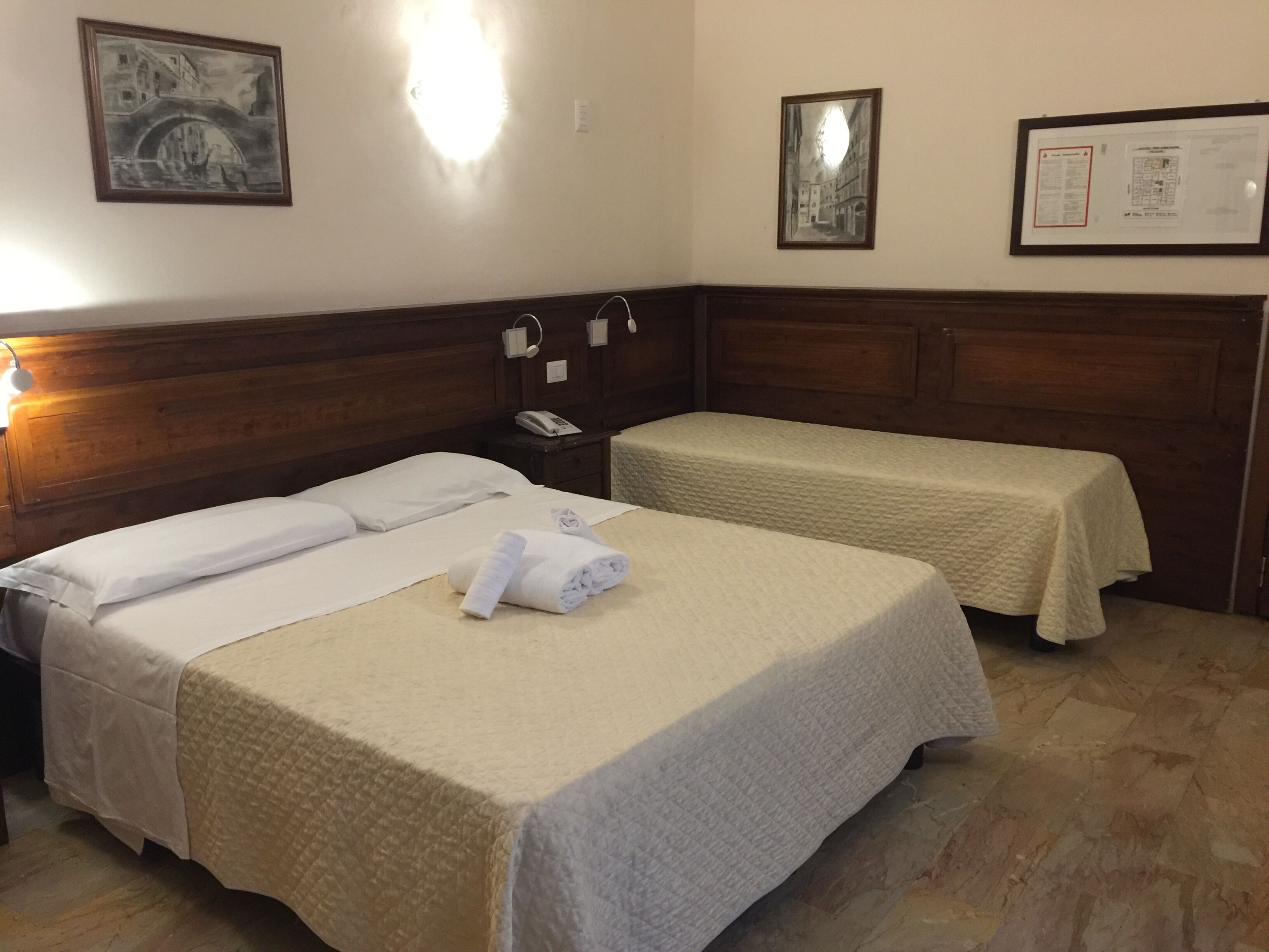 A hotel room with two beds, a wooden headboard, a nightstand, and a wall-mounted phone.