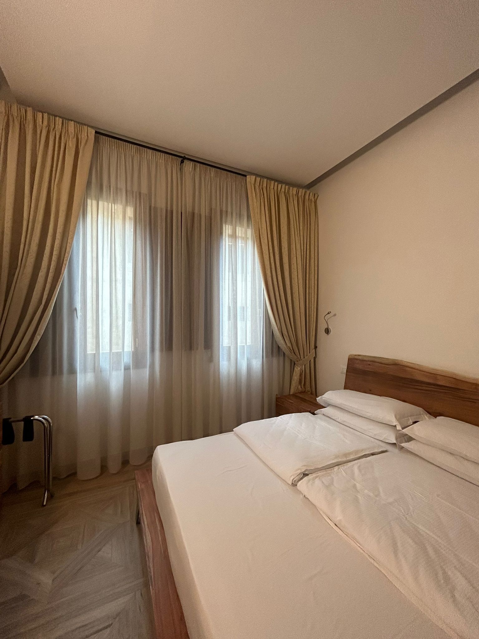 A hotel room with a bed, curtains, a wooden headboard, and a wooden floor.