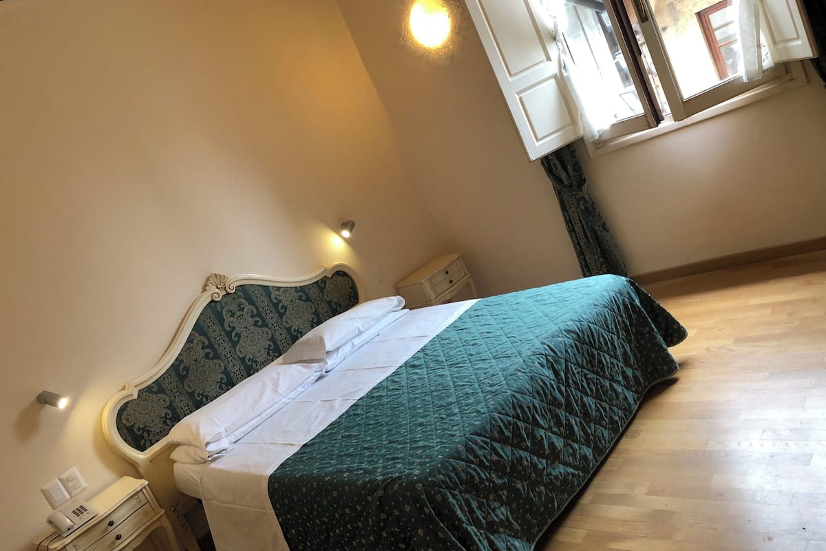 A neatly made bed with a green bedspread and white linens in a room with wooden flooring.