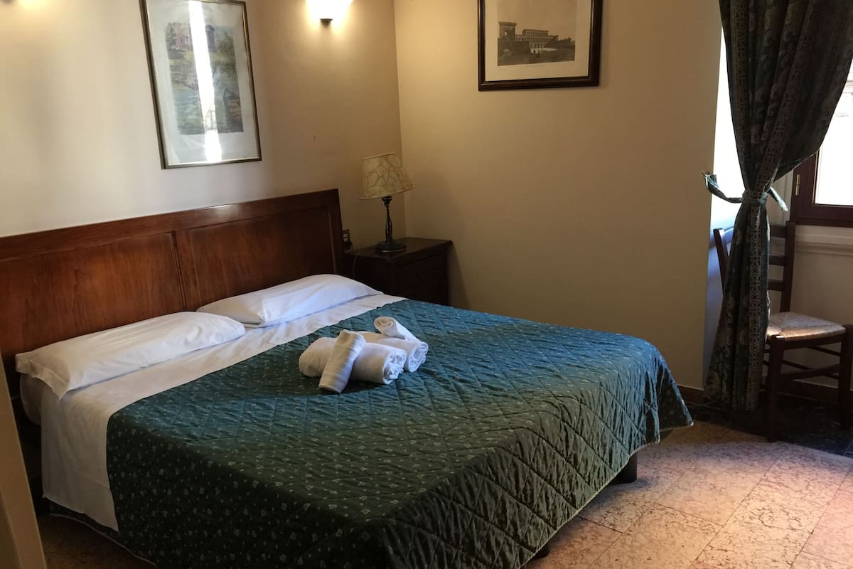 A neatly made bed with a green quilt, a wooden headboard, and two framed pictures on the wall.