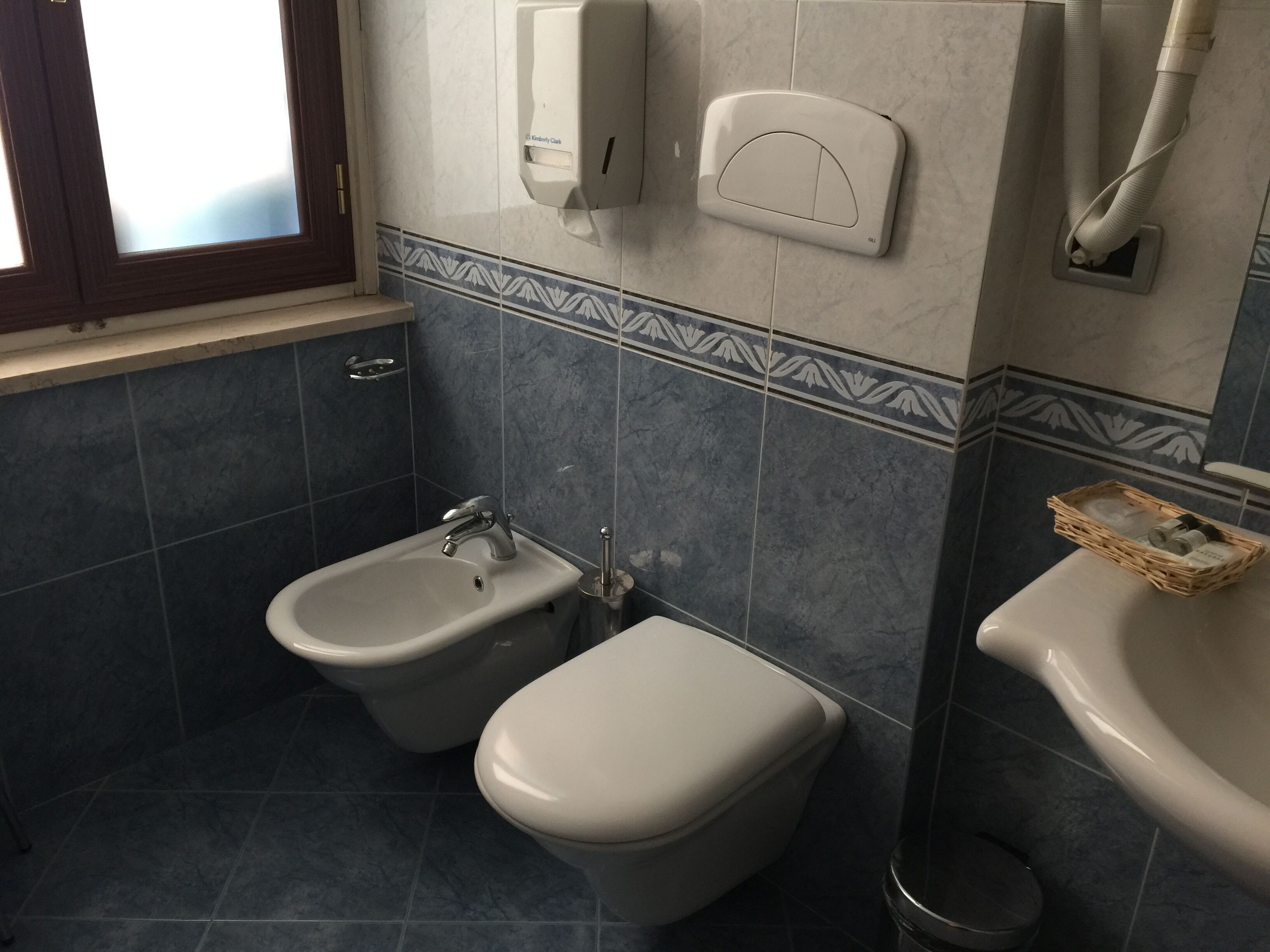 A bathroom with a bidet, a toilet, a sink, and a hand dryer.