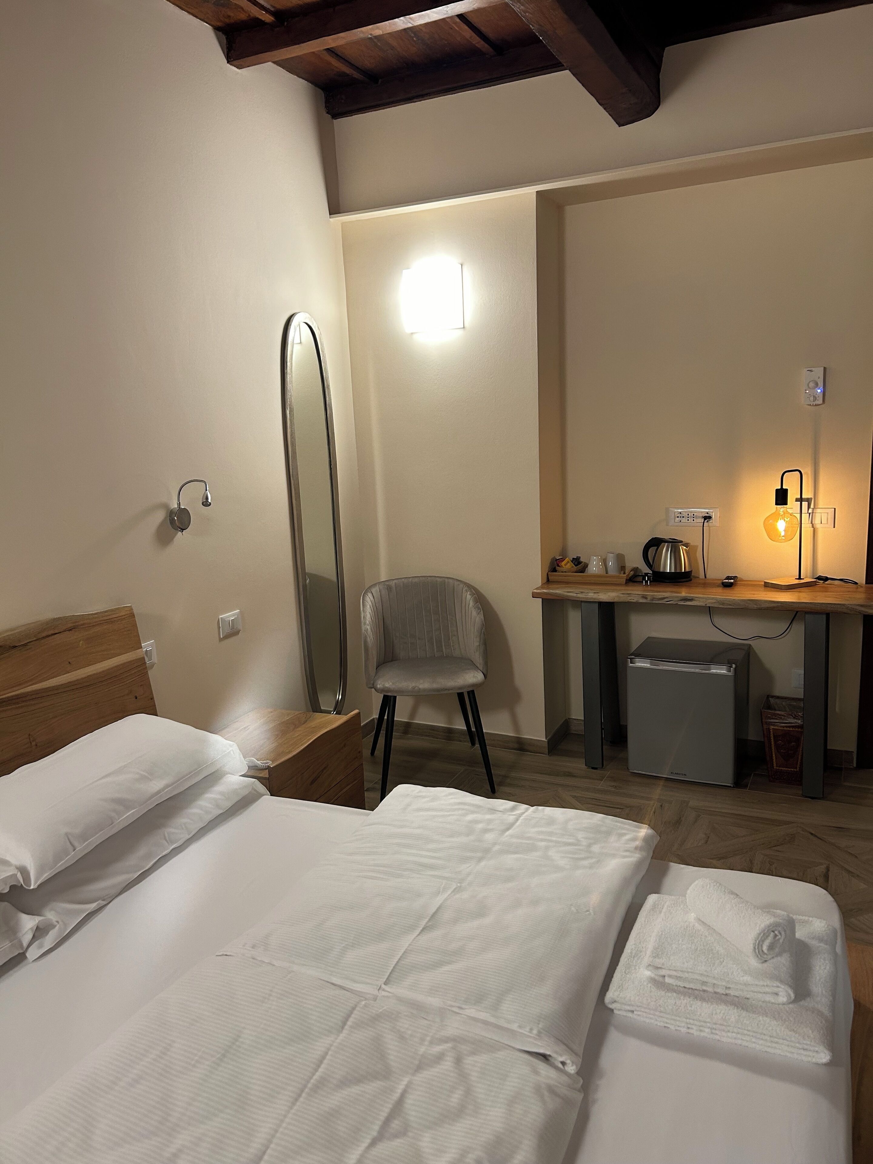 A hotel room with a bed, a desk, a chair, a mirror, and a small refrigerator.