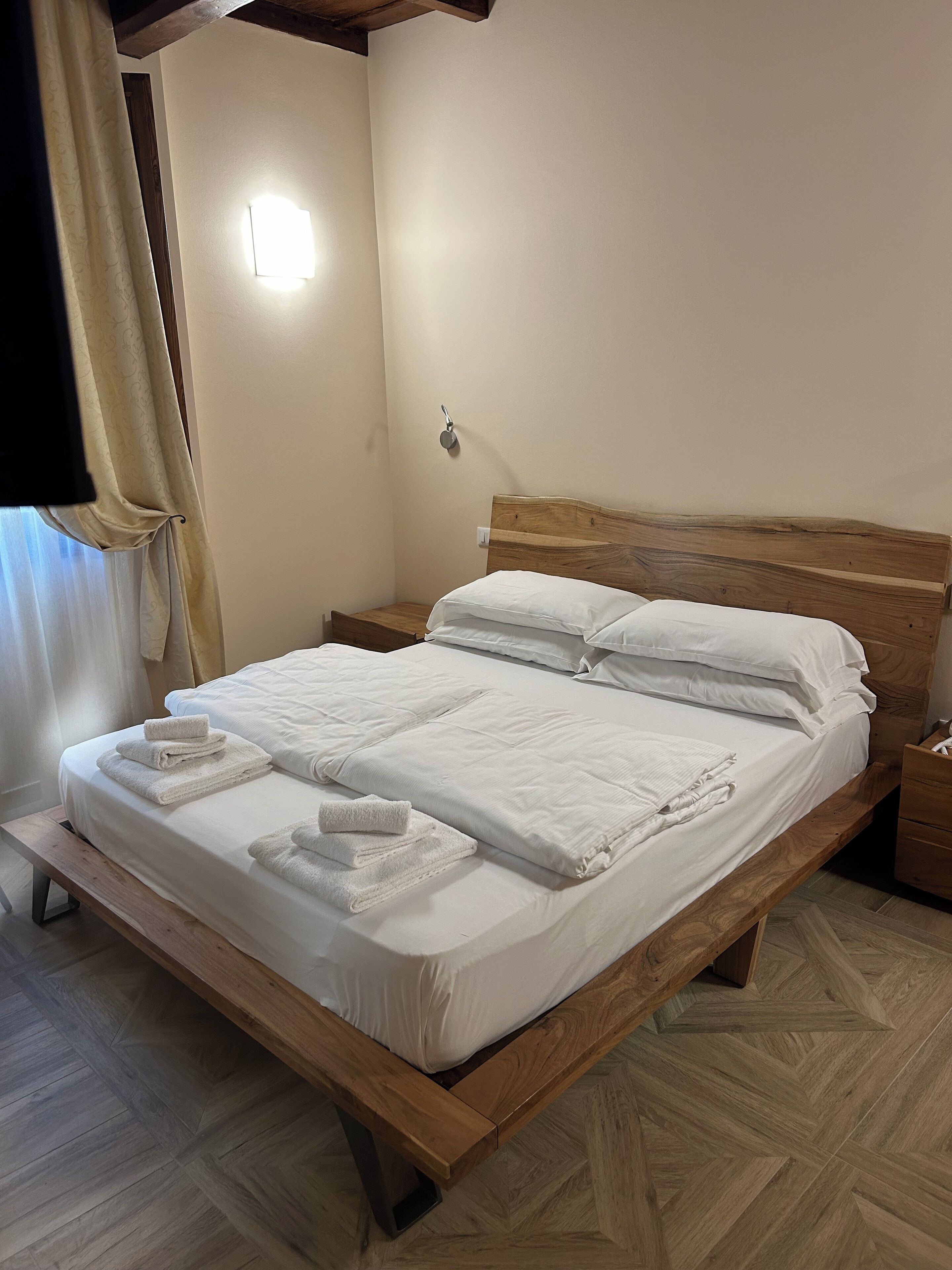 A neatly made bed with white linens and towels, a wooden headboard, and a bedside table with a lamp.