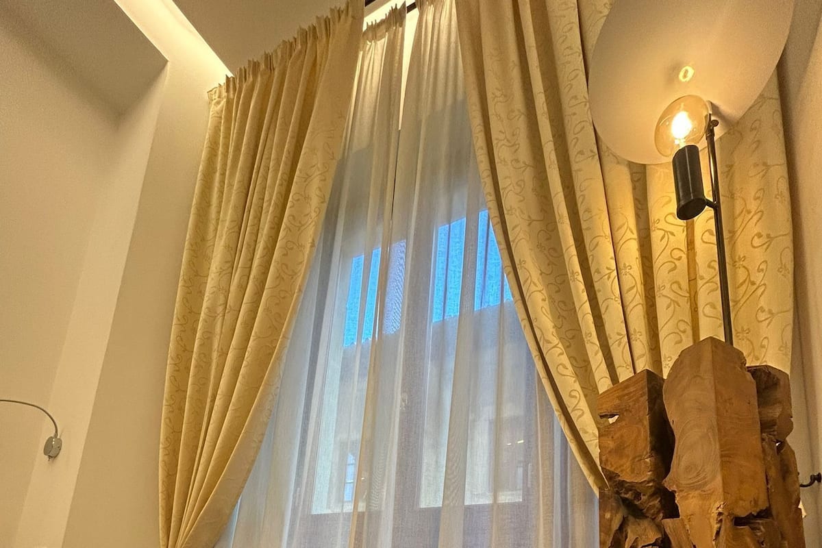 A modern bedroom with a bed, two chairs, a stone accent wall, and sheer curtains.