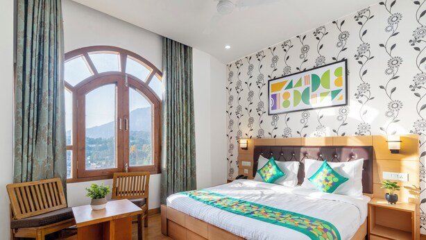 A bedroom with a large bed, a wooden desk, and a window with curtains. - Treebo Anand The Mall Solan (Solan)