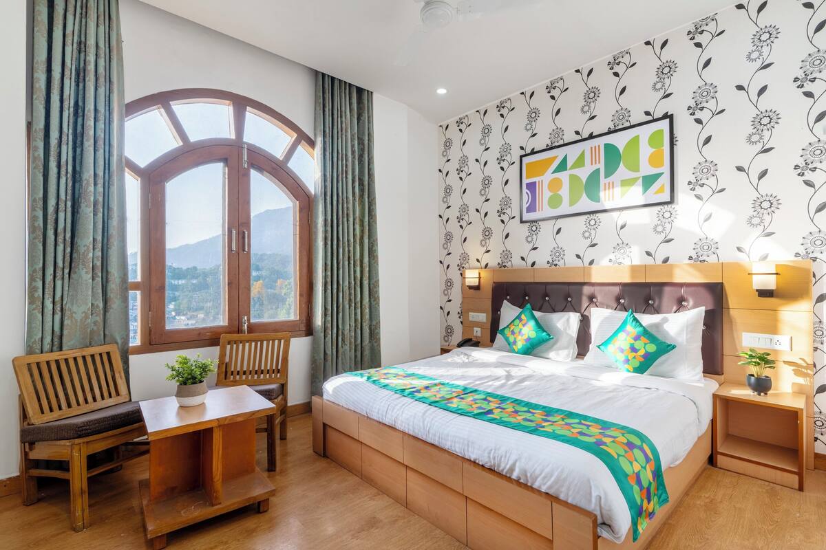 A bedroom with a large bed, a wooden desk, and a window with curtains.