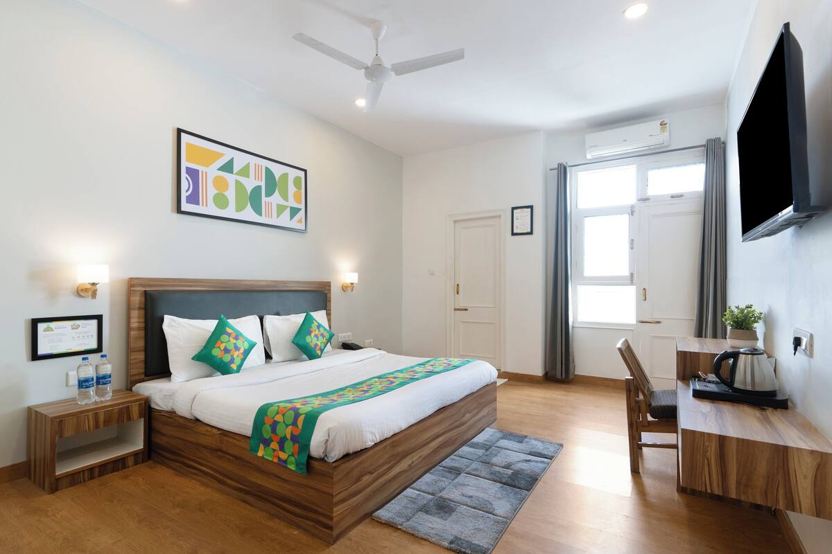 A modern hotel room with a wooden bed, a desk, a chair, and a flat-screen TV.