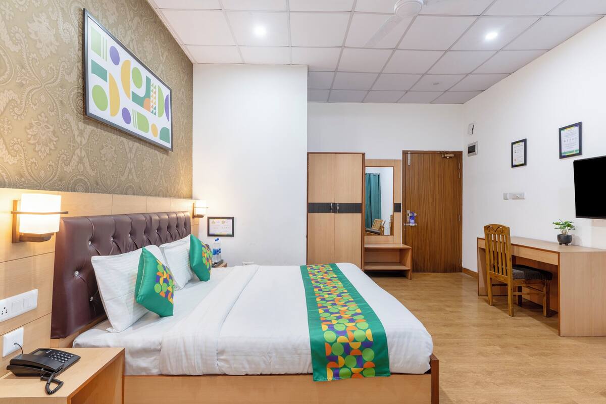 A hotel room with a bed, bedside table, desk, chair, and a mirror.