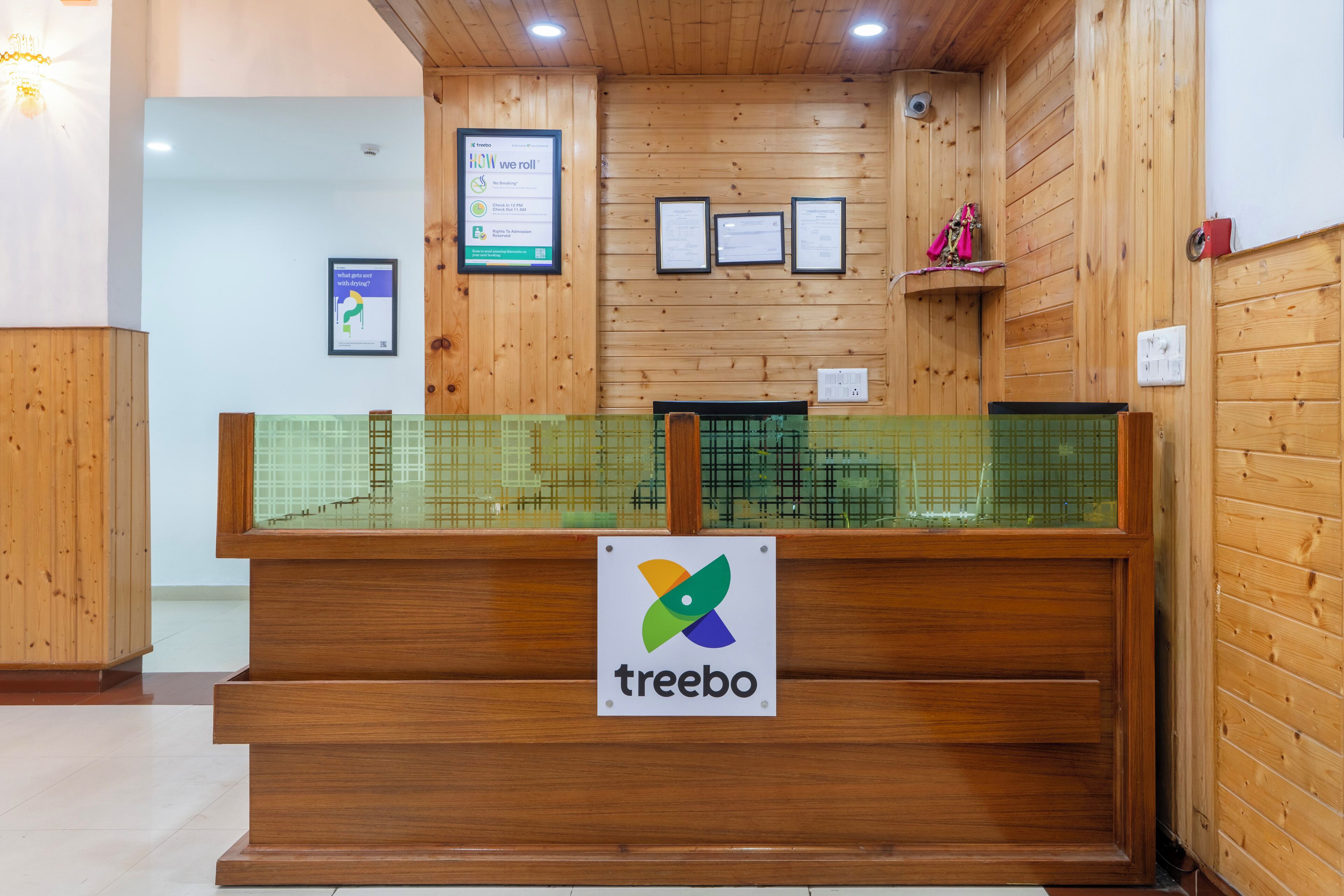 Ein Empfangsschalter mit einem 'Treebo'-Schild, Holzwänden, gerahmten Zertifikaten und einer grün gefliesten Theke.