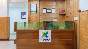 Ein Empfangsschalter mit einem 'Treebo'-Schild, Holzwänden, gerahmten Zertifikaten und einer grün gefliesten Theke.