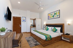 A modern bedroom with a wooden bed, a flat-screen TV, a ceiling fan, and a large abstract painting. - Treebo Anand The Mall Solan (Solan)