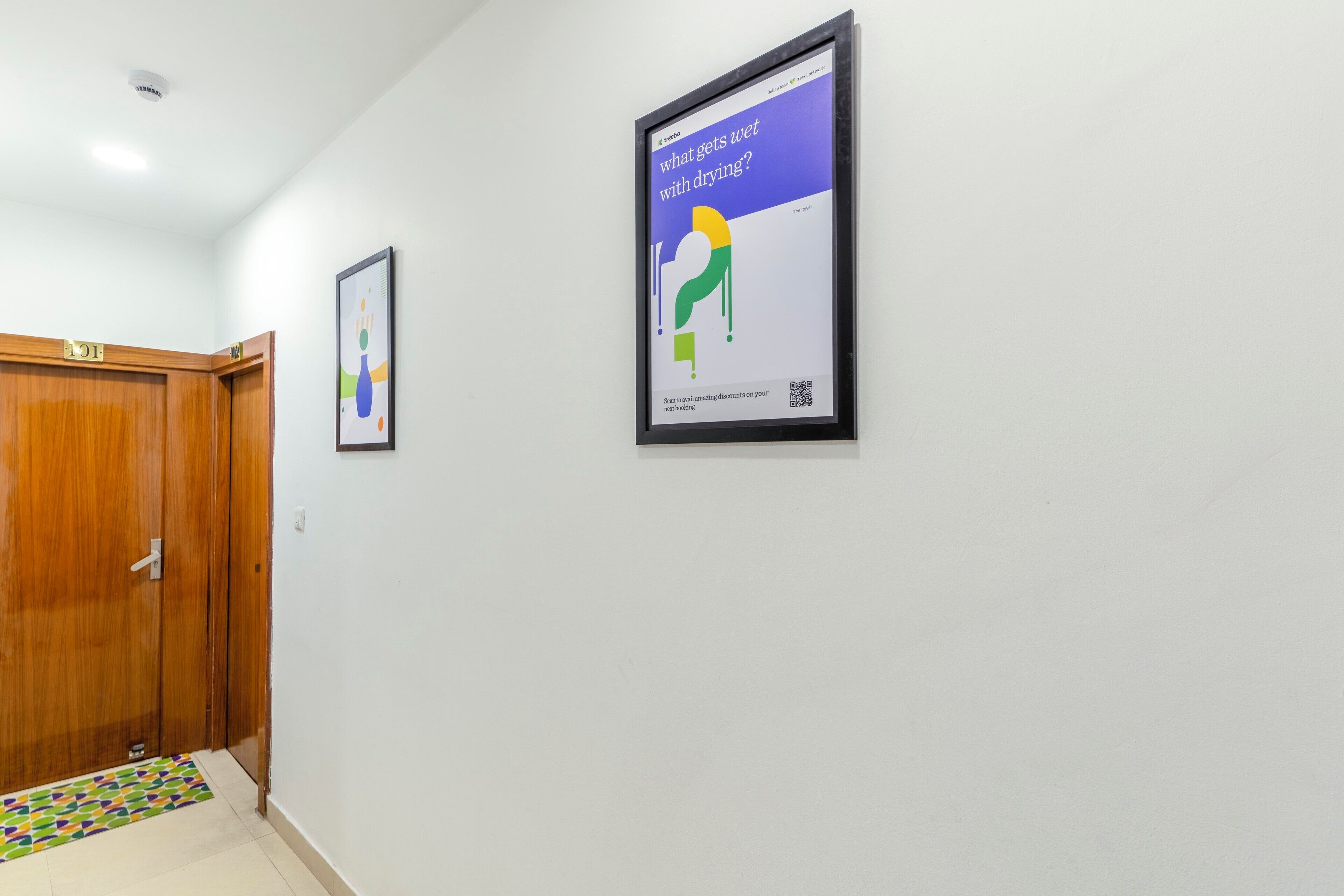 Un pasillo con una puerta de madera, un felpudo colorido y un cartel en la pared.