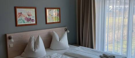 Un dormitorio con una cama, dos almohadas, una lámpara de noche y dos obras de arte enmarcadas en la pared.