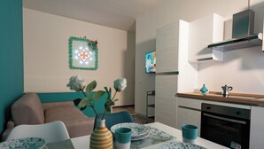 Una cocina moderna con zona de comedor, un sofá y un televisor montado en la pared.