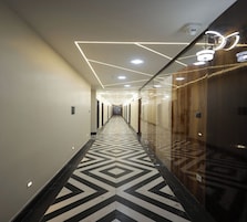 En moderne hotelgang med geometrisk gulvbelægning, indbygget belysning og en glas elevator.
