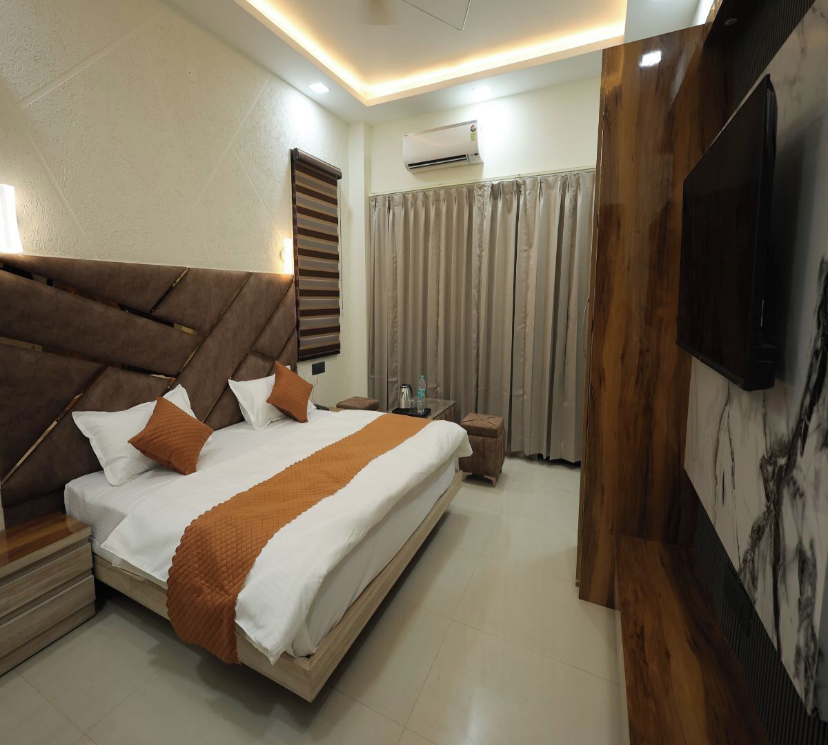 Una habitación de hotel moderna con una cama grande, cabecera de madera, televisión de pantalla plana y equipo de aire acondicionado.