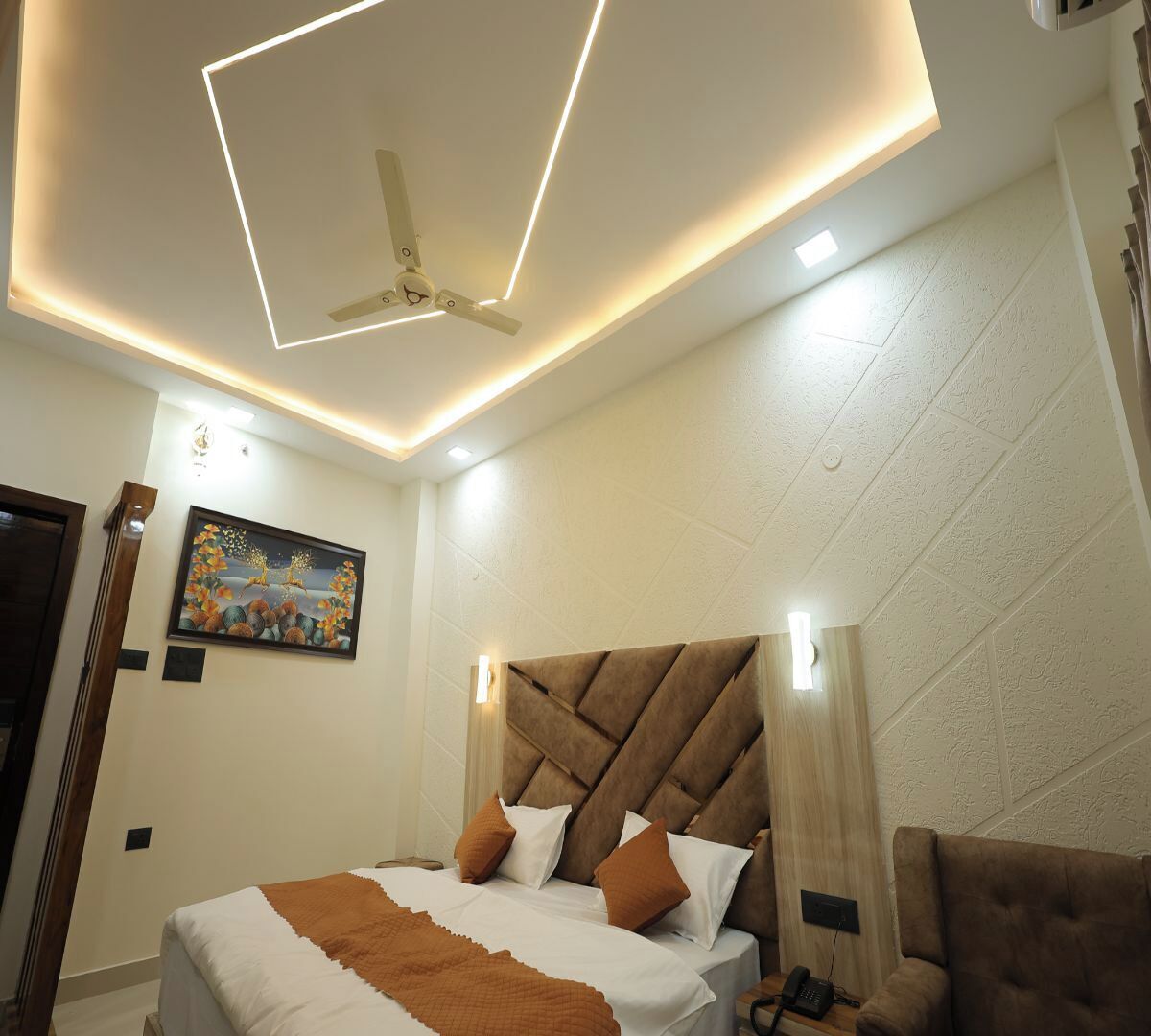 A modern bedroom with a large bed, a ceiling fan, recessed lighting, a painting on the wall, and a wooden headboard.